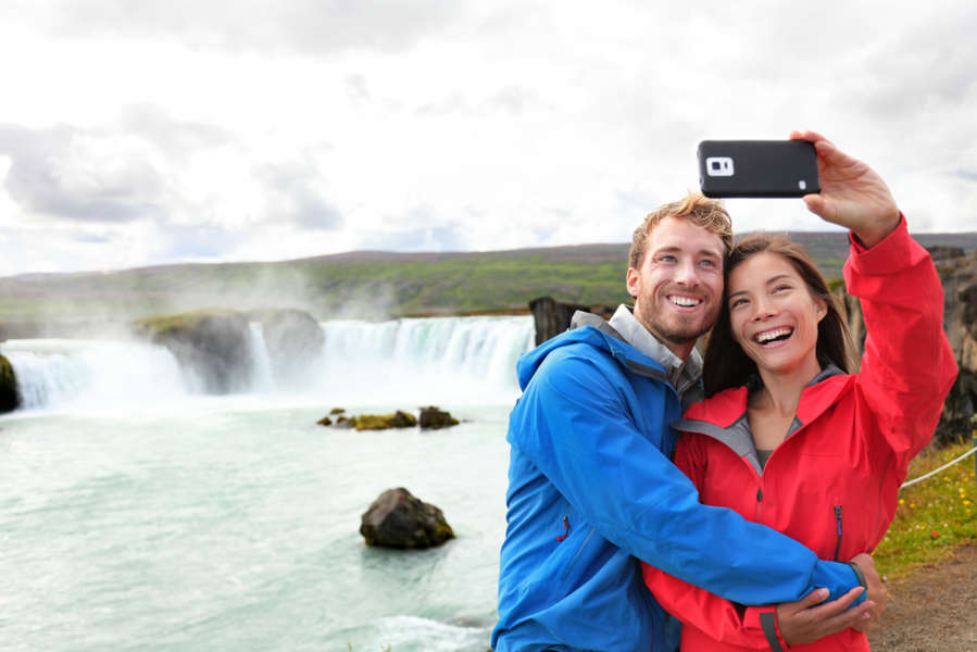 Couple utilisant les réseaux mobiles en Islande et se prenant en photo devant une cascade