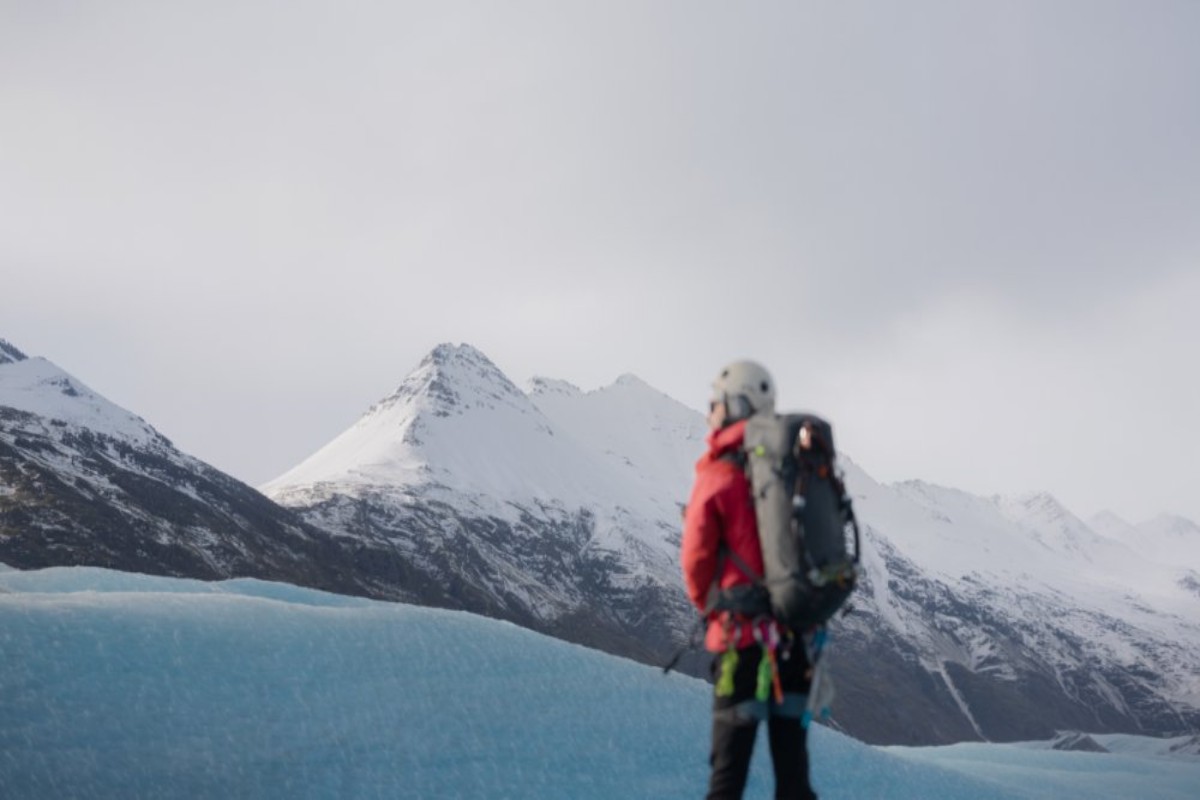 Randonneur sur glacier en veste rouge à côté de glace bleue avec des montagnes islandaises enneigées en arrière-plan
